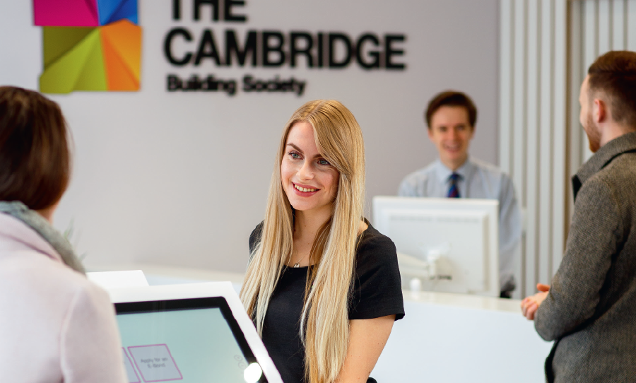 Staff assisting customers inside a Cambridge Building Society branch, with the company’s signage visible in the background.