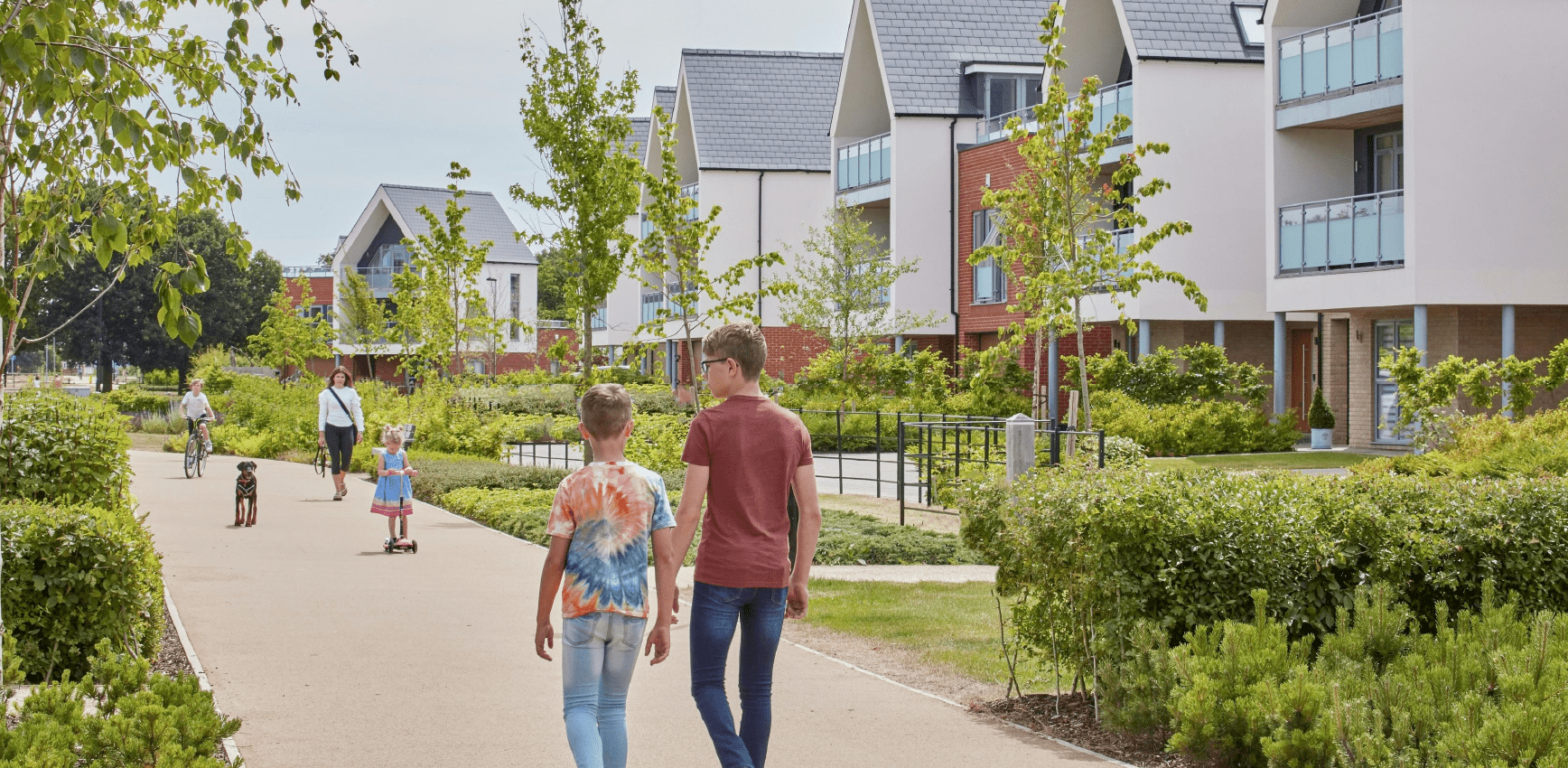 People walk, cycle, and play along a landscaped pathway in a modern residential neighbourhood with contemporary homes and greenery.