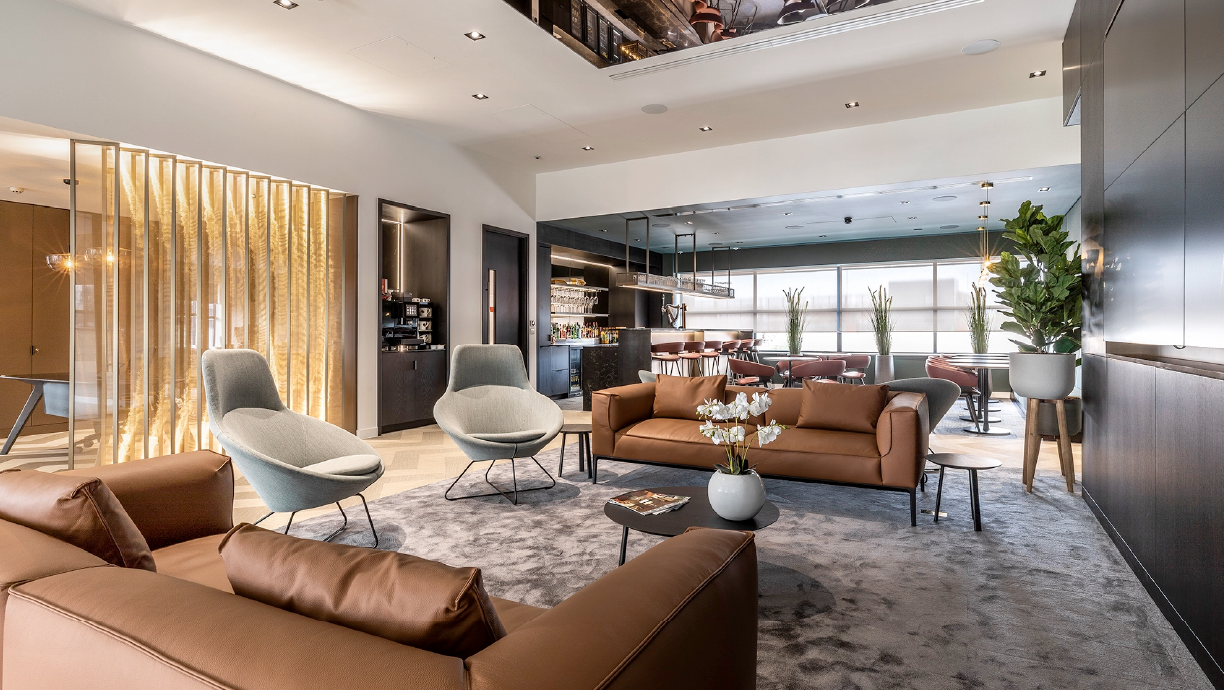 Modern office lounge with sofas, chairs, and a bar area.