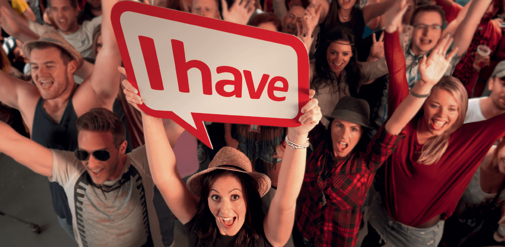 A raised view of a crowd of young people with raised arms. The girl at the front is holding a speech bubble sign saying, "i have".
