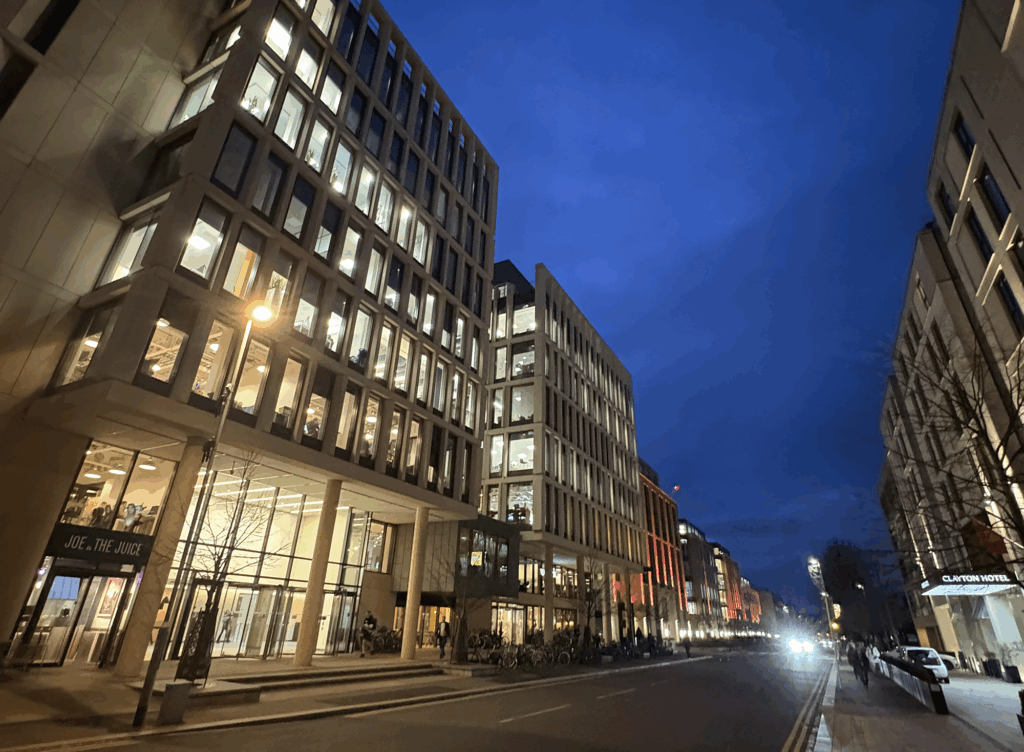 Station Road in Cambridge at dusk, with modern office buildings illuminated along the street.
