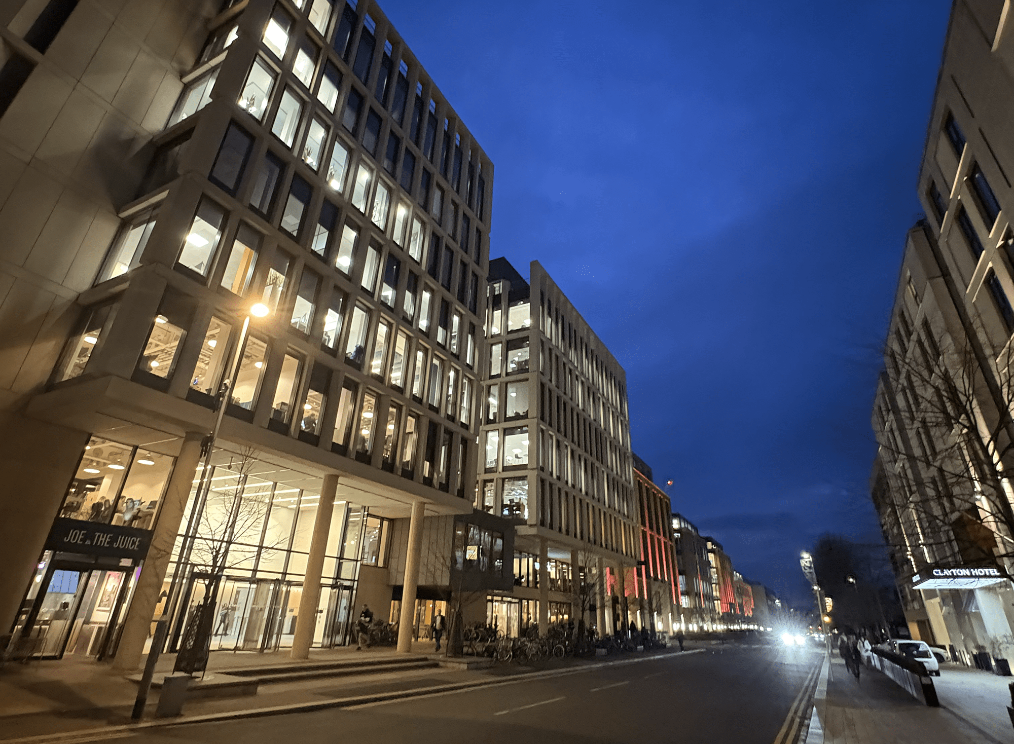 Station Road in Cambridge at dusk, with modern office buildings illuminated along the street.