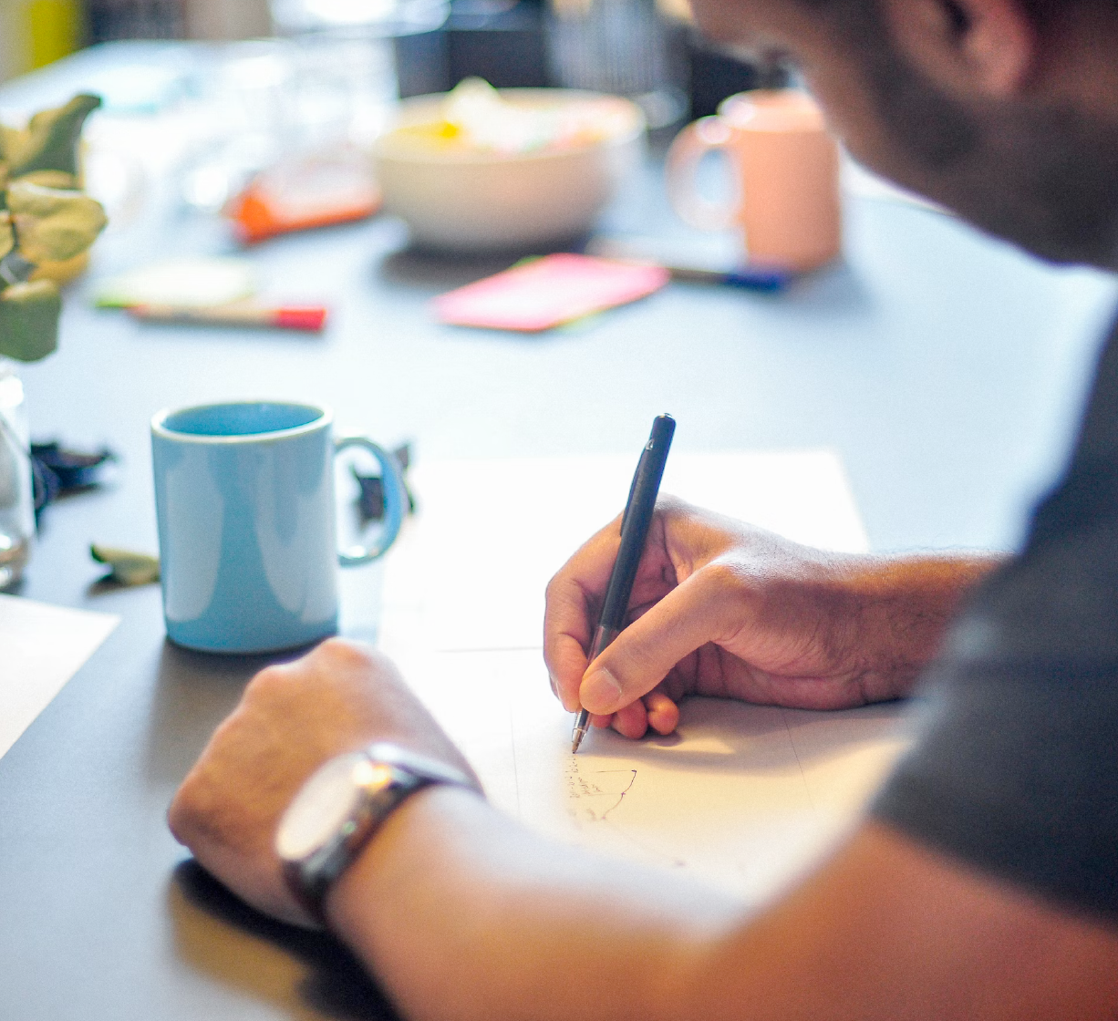 Person writing notes on paper at a desk with a coffee mug nearby