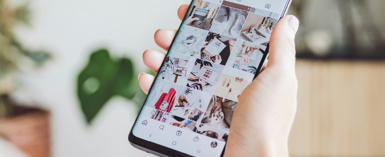 Hand holding a smartphone displaying a grid of lifestyle and product photos on a social media app.