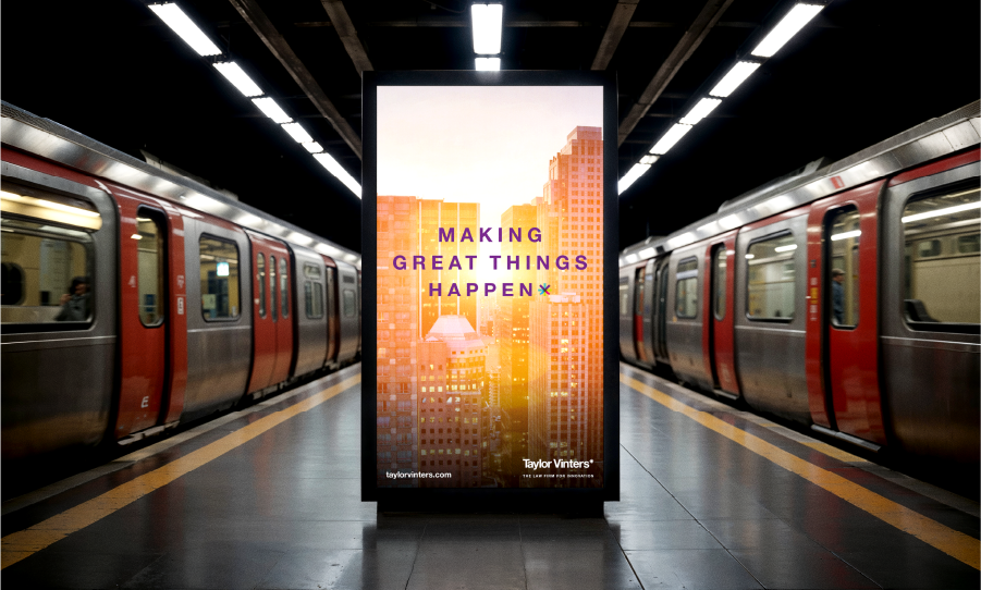 A digital poster in a subway station displays the message “Making Great Things Happen” against a cityscape background, with trains on both sides of the platform.