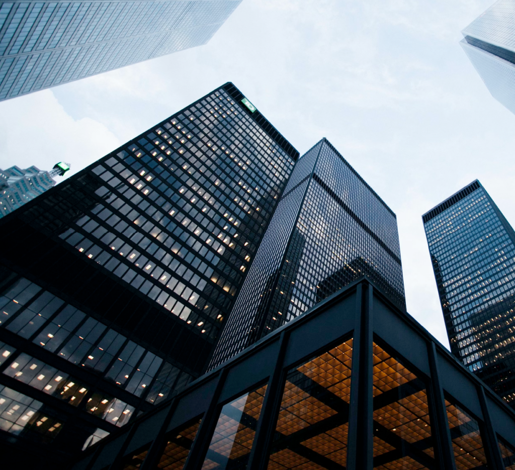 Upward view of tall modern skyscrapers with glass and steel facades against a bright sky.