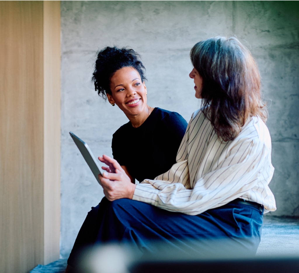 Two people sitting together indoors, looking at a tablet device.