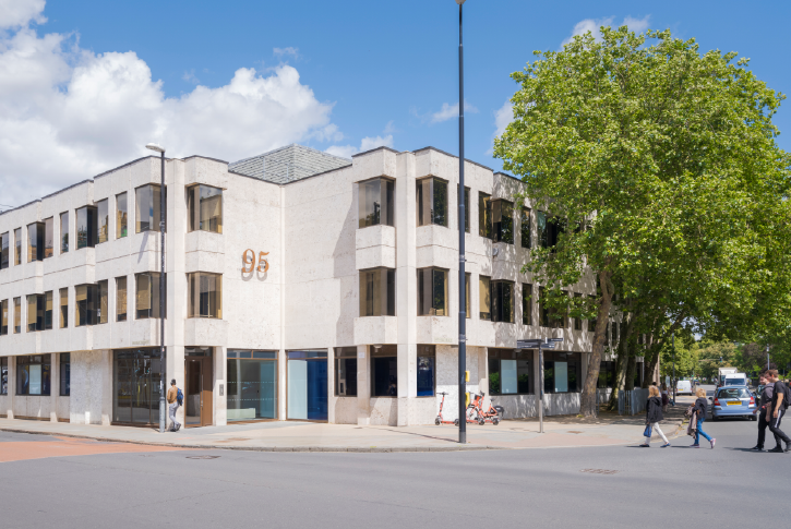 Exterior view of the Mobas office at 95 Regent Street, Cambridge, showing a modern light‑coloured corner building with large windows and a tree‑lined street.