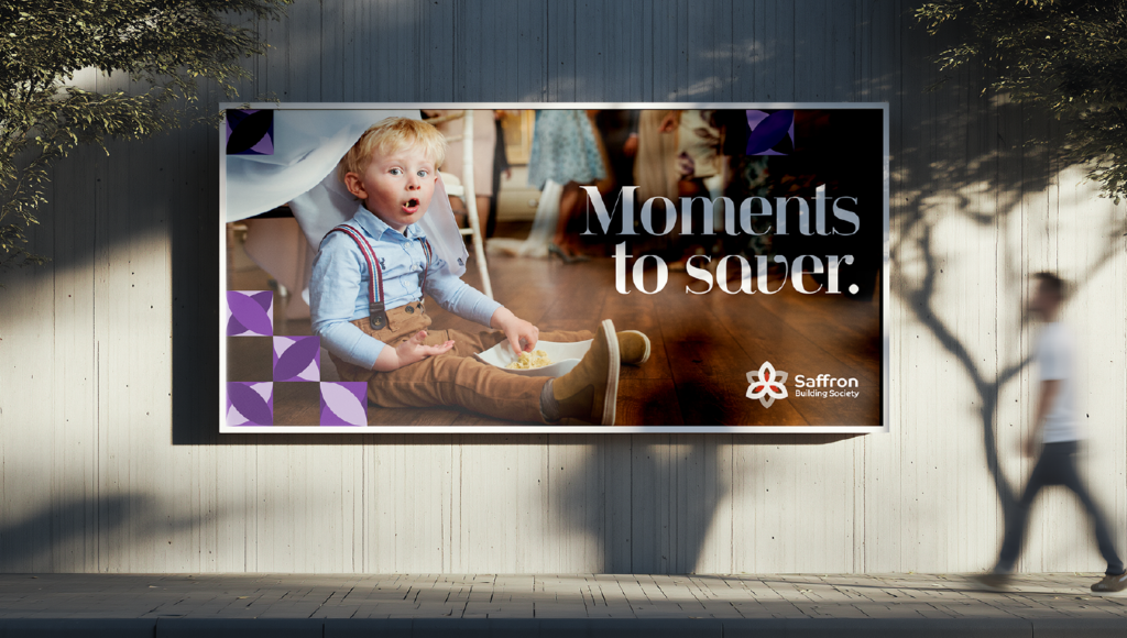 A Saffron Building Society billboard showing a child sitting on a wooden floor at an event, with the headline “Moments to saver.”