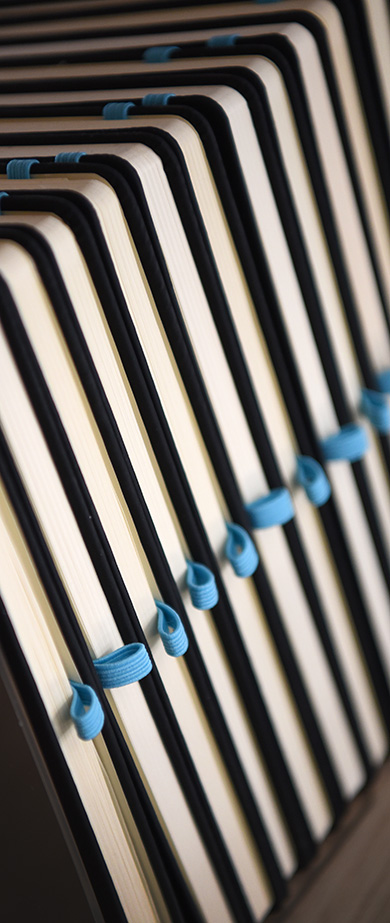 Close‑up view of neatly stacked notebooks with black spines and blue ribbon pen holding loops.