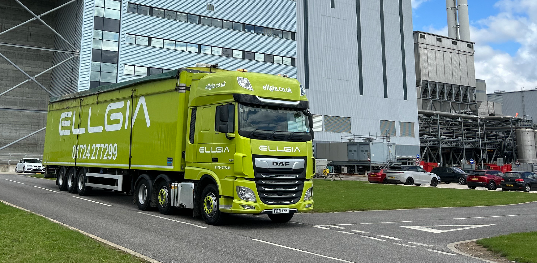 Bright green Ellgia truck on a road outside a large industrial plant.