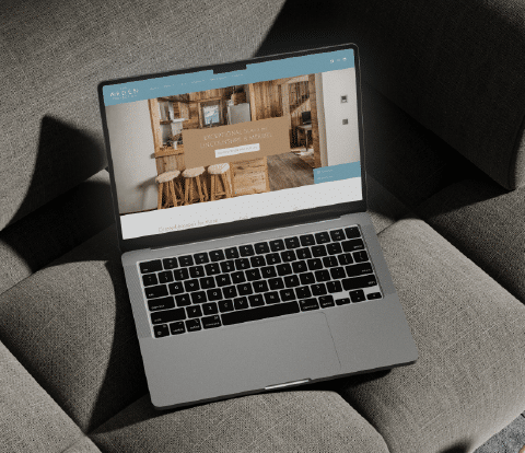 Laptop displaying The Arden Collection website homepage on a sofa.
